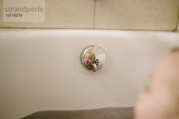 Spiegelung eines Mädchens im Druckknopf einer Badewanne