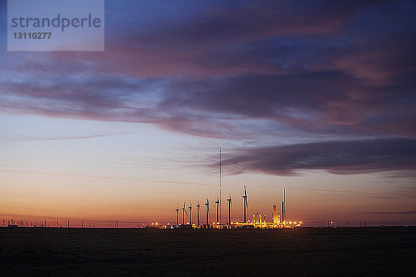 Beleuchtetes Kraftwerk gegen bewölkten Himmel in der Dämmerung