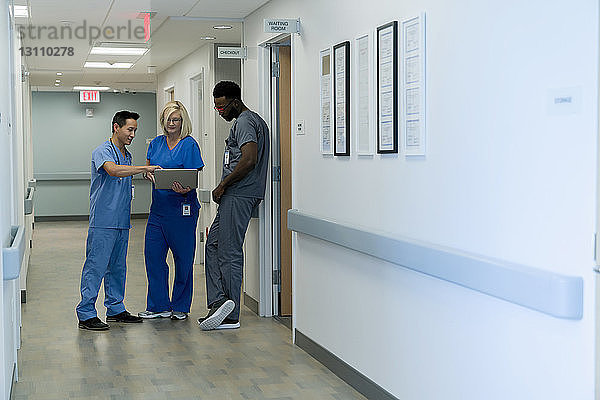 Ärzte diskutieren über Laptop-Computer  während sie im Krankenhauskorridor stehen
