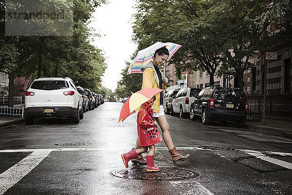 Seitenansicht von Mutter und Tochter  die beim Überqueren der Straße Regenschirme halten