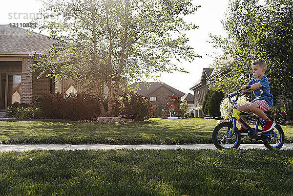 Seitenansicht eines Jungen  der auf der Straße inmitten eines Grasfeldes Fahrrad fährt