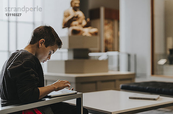 Seitenansicht eines Jungen  der einen Tablet-Computer benutzt  während er zu Hause sitzt