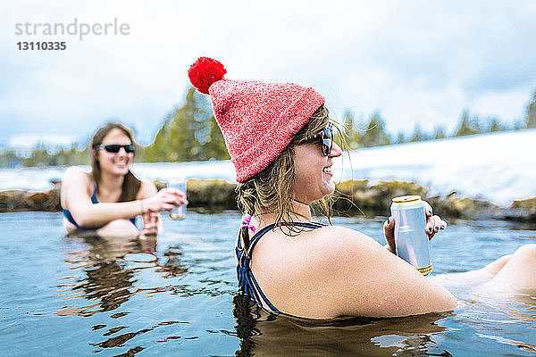 Glückliche Freundinnen genießen im Winter Getränke im See
