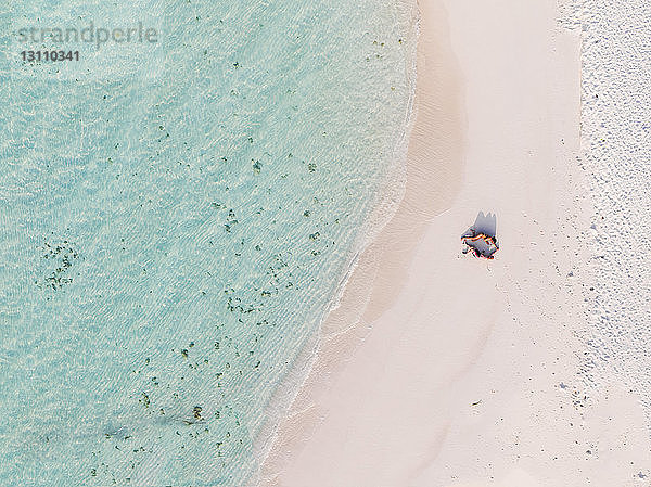 Luftaufnahme eines am Sandstrand liegenden Paares