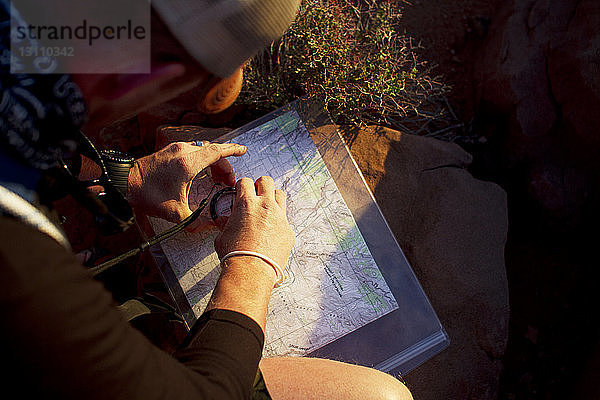 Draufsicht auf den Menschen mit Navigationskompass auf der Karte  während er auf dem Feld sitzt