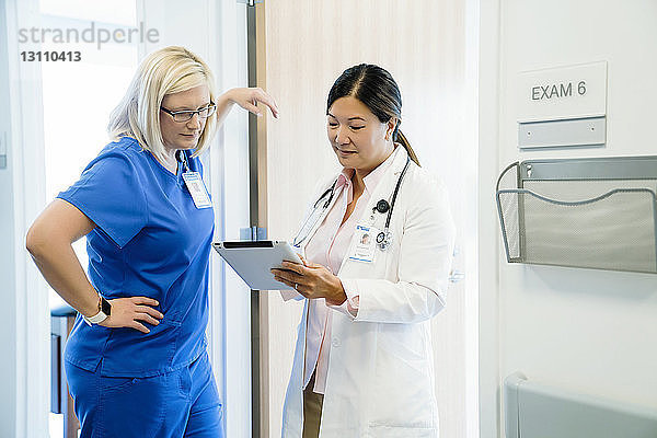 Ärztinnen schauen auf Tablet-Computer  während sie im Krankenhaus an der Wand stehen