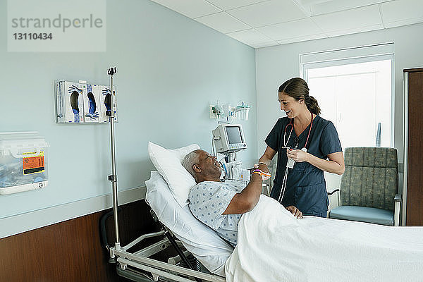 Händeschütteln einer Krankenschwester mit einem älteren Patienten  der auf der Krankenhausstation auf dem Bett liegt