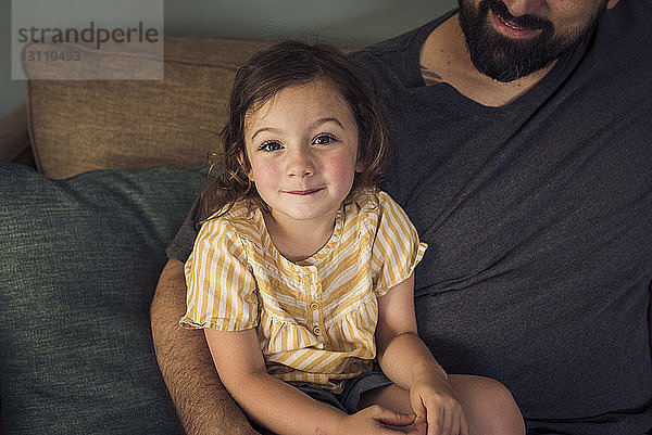 Hochwinkelporträt eines Mädchens  das mit seinem Vater zu Hause auf dem Sofa sitzt