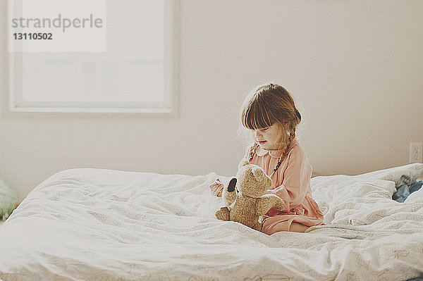Süßes Mädchen spielt mit Teddybär auf dem Bett