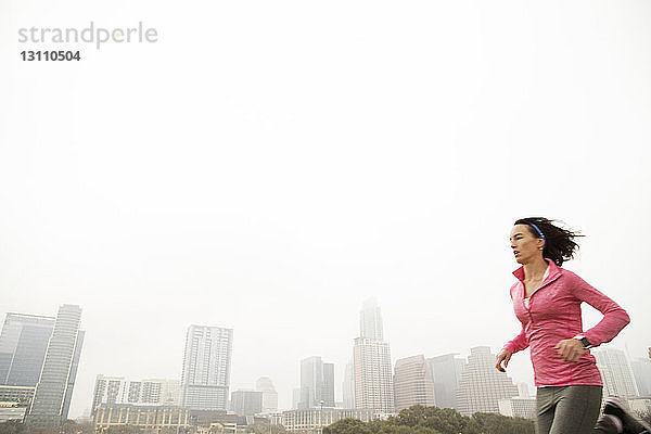 Frau joggt in der Stadt gegen den Himmel