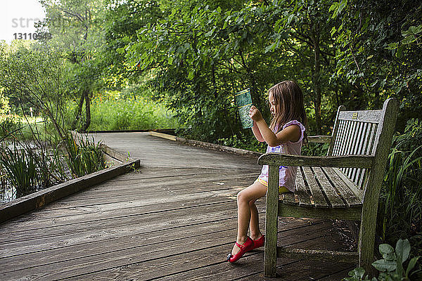 Seitenansicht eines Mädchens  das auf einer Parkbank sitzend ein Buch liest