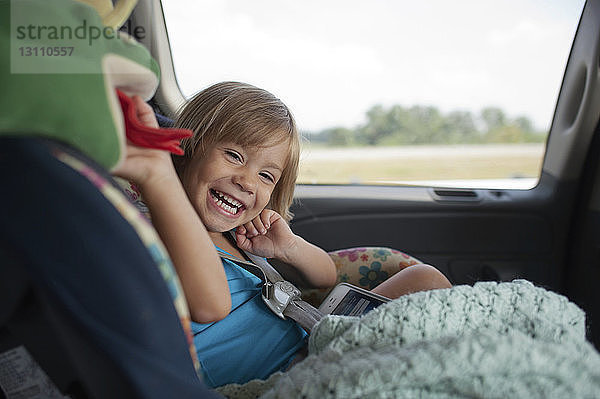 Porträt eines glücklichen Mädchens mit Handy im Auto unterwegs