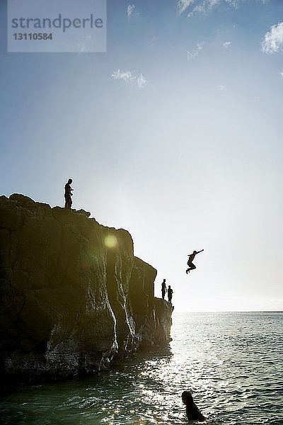 Freunde springen von Felsformation ins Meer