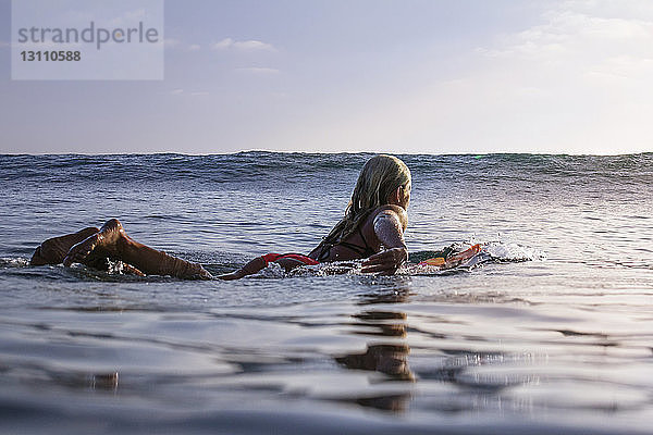 Frau schwimmt auf einem Surfbrett im Meer gegen den Himmel