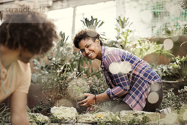 Glückliche Frau schaut Freundin bei der Gartenarbeit im Gemeinschaftsgarten an