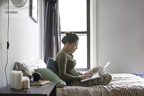 Frau benutzt Laptop  während sie zu Hause auf dem Bett sitzt