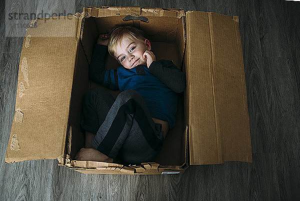 Hochwinkelporträt eines Jungen  der zu Hause in einem Pappkarton liegt