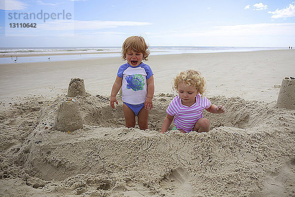 Junge weint  während Mädchen am Strand mit Sand spielt