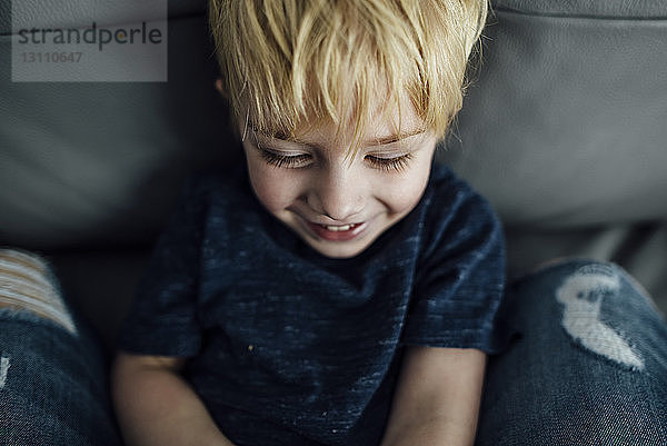 Hochwinkelaufnahme eines lächelnden Jungen  der zu Hause auf dem Sofa sitzt