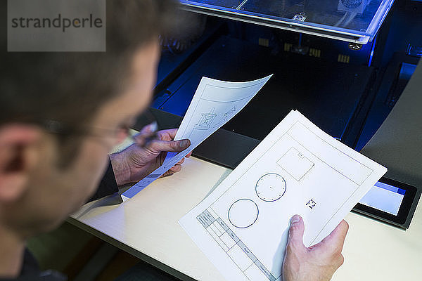 Ingenieur hält Dokumente per 3D-Drucker am Tisch im Büro