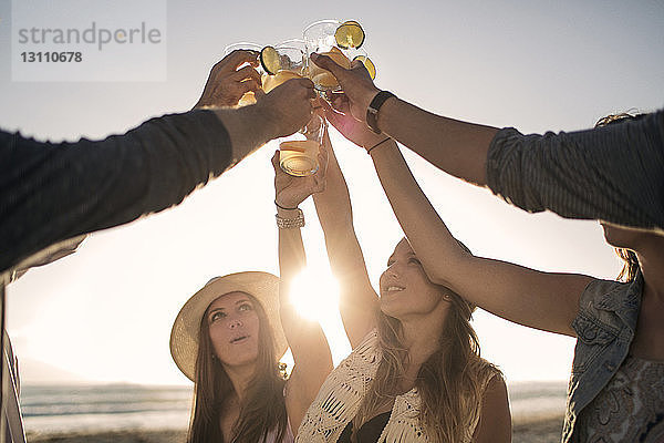 Glückliche Freunde stoßen am Strand auf Getränke an