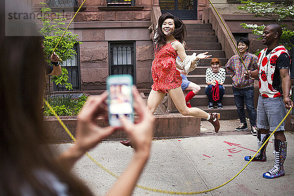 Frau fotografiert Freunde  die auf dem Bürgersteig Doppel-Holländisch spielen