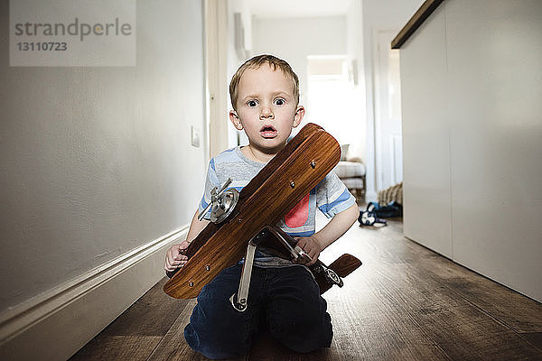 Porträt eines überraschten Jungen  der zu Hause kniend ein Modellflugzeug hält