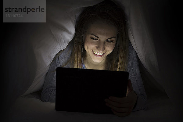 Glückliche Frau benutzt Laptop-Computer  während sie in einer Decke liegt