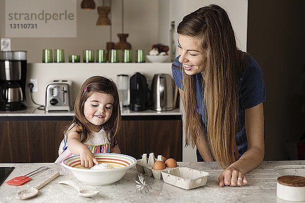 Mutter sieht Tochter beim Spielen mit Mehl auf Kücheninsel