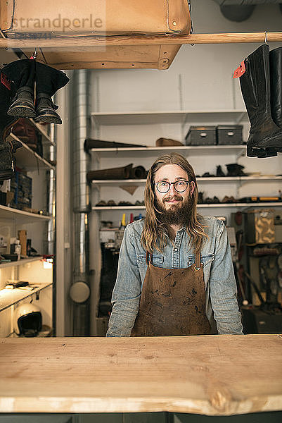 Porträt eines lächelnden Schuhmachers  der an der Werkbank in der Werkstatt steht