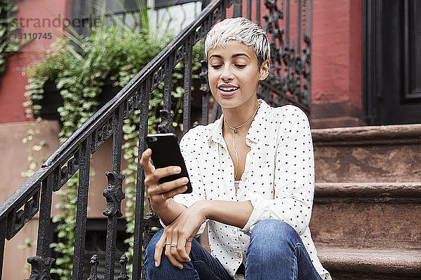 Glückliche Frau benutzt Mobiltelefon  während sie auf einer Treppe sitzt
