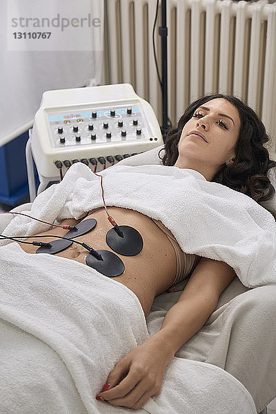 Hochwinkelansicht eines Patienten mit Elektroden Physiotherapie im Liegen in einer medizinischen Klinik