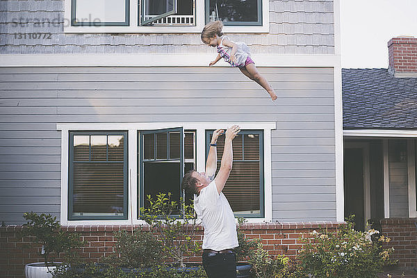 Verspielter Vater wirft Tochter in die Luft  während er im Hinterhof steht