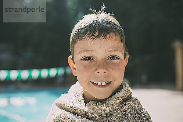 Porträt eines in ein Handtuch gewickelten glücklichen Jungen am Poolufer stehend
