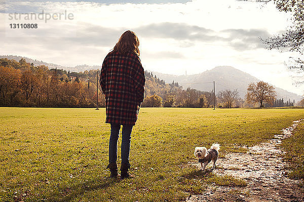 Rückansicht von Frau und Hund auf Grasfeld stehend gegen den Himmel