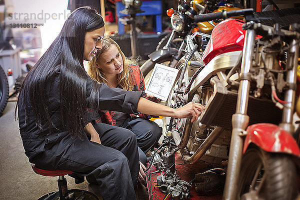 Mechanikerinnen mit digitalem Tablett bei Fahrradreparaturen in der Werkstatt