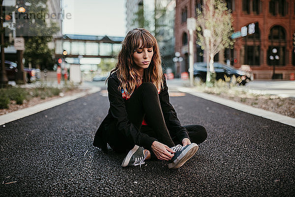 Junge Frau bindet Schnürsenkel  während sie auf der Straße in der Stadt sitzt