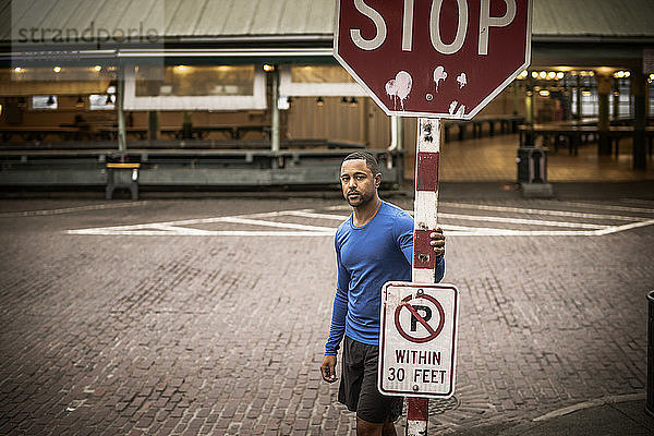 Porträt eines Athleten  der an einem Stoppschild auf der Strasse steht
