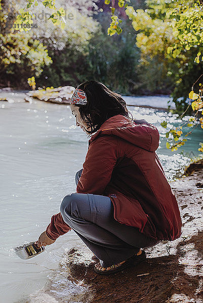 Frau nimmt Wasser in Behälter aus fließendem Fluss im Wald