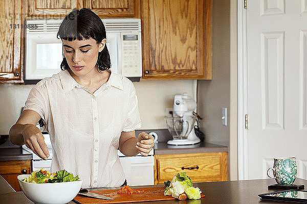 Frau würzt Salat  während sie zu Hause in der Küche steht