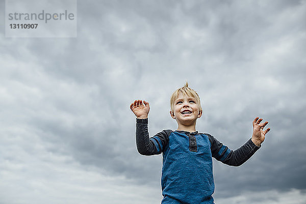 Tiefwinkelansicht eines fröhlichen Jungen  der vor bewölktem Himmel steht