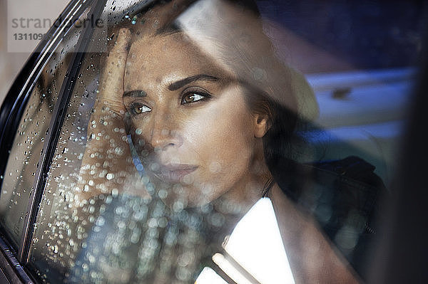 Nachdenkliche Frau schaut durch das Fenster  während sie im Auto sitzt