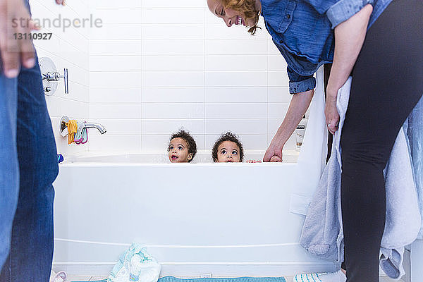 Glückliche Mutter schaut auf niedliche Töchter  die in der Badewanne sitzen