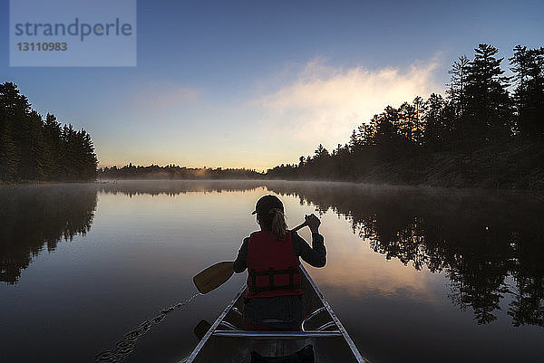 Rückansicht einer Frau  die bei Sonnenuntergang in einem Boot auf einem ruhigen See reist