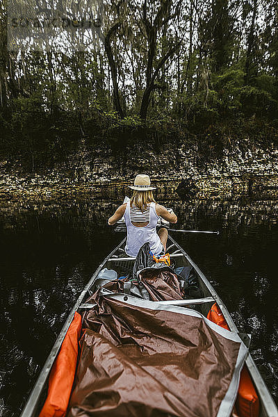Rückansicht einer jungen Frau beim Kanufahren auf einem See im Wald
