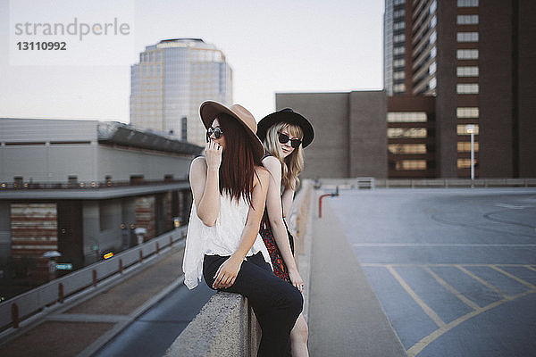 Freunde sitzen auf der Stützmauer einer Gebäudeterrasse in der Stadt