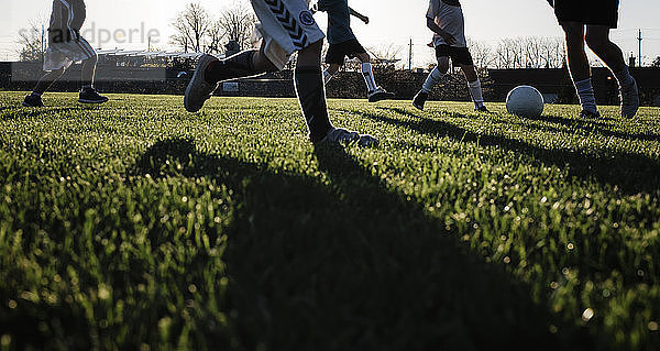 Niedriger Teil eines Mannes  der bei Sonnenuntergang mit Kindern auf einem Rasenfeld im Park Fussball spielt