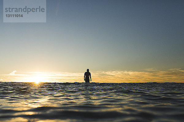 Fernblick einer Surferin auf dem Meer gegen den Himmel bei Sonnenuntergang