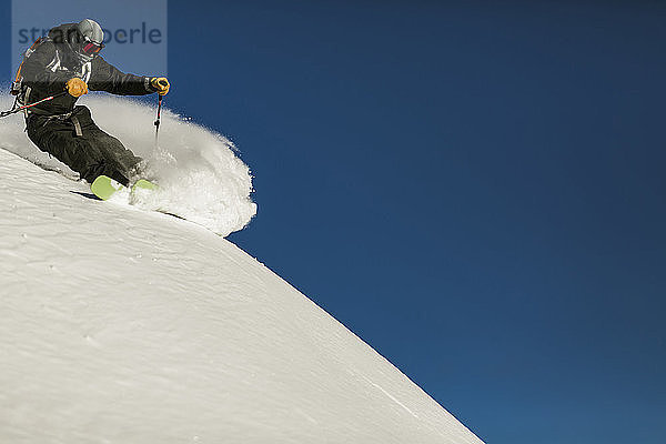 Tiefwinkelaufnahme eines Mannes beim Skifahren auf einem schneebedeckten Berg vor klarem  blauem Himmel