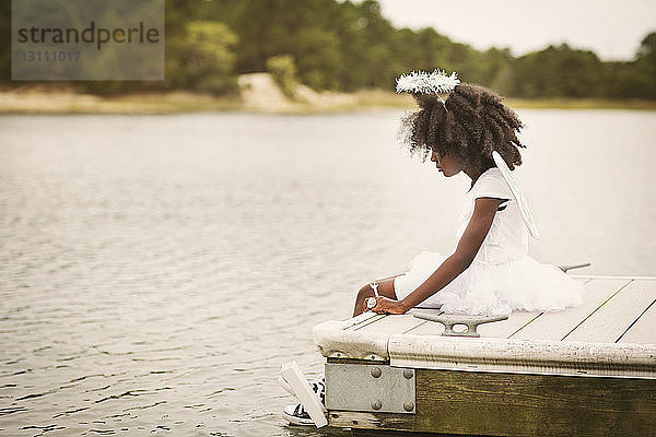 Seitenansicht eines Mädchens  das auf einem Pier am See sitzt
